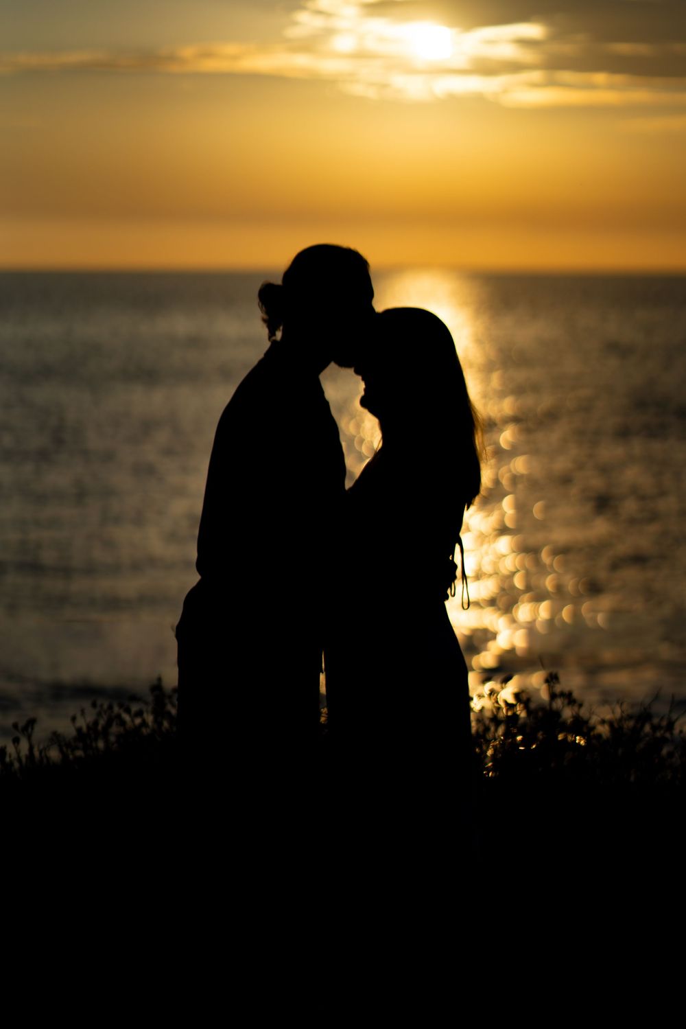 Romantic silhouette of a couple kissing against a golden ocean sunset backdrop. San Diego CA Sunset Cliffs