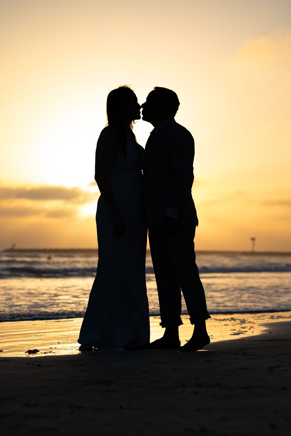 Silhouette of a couple sharing a romantic kiss on the beach at sunset with golden ocean backdrop. Oceanside, CA