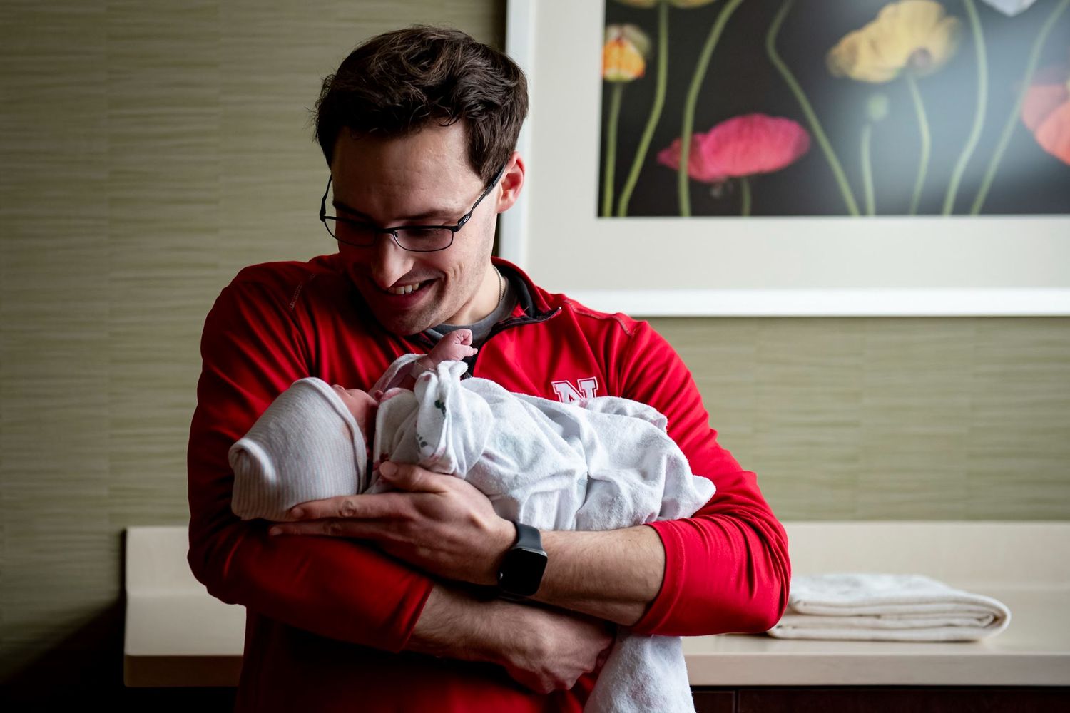 A person in red sweater gazes lovingly at a sleeping newborn baby wrapped in white.