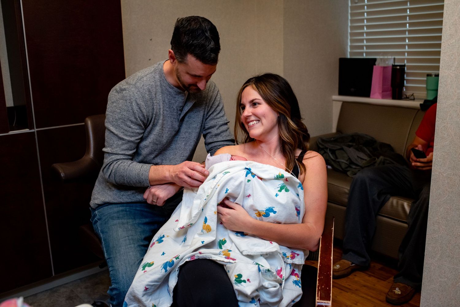 Parents admire their newborn baby wrapped in a blue patterned blanket in a hospital room.