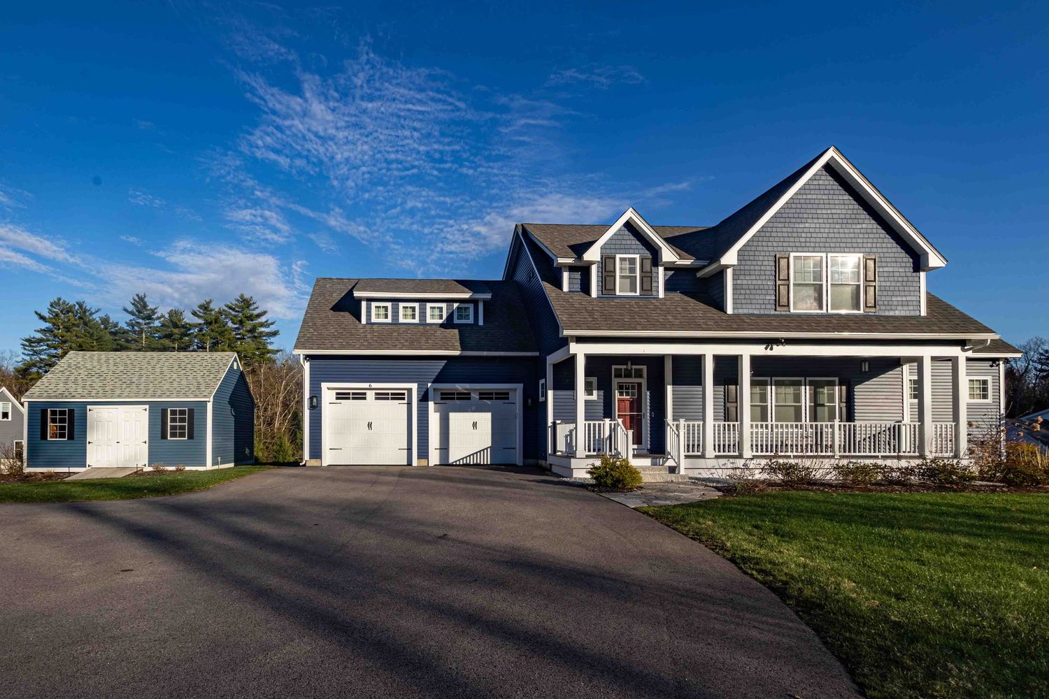 Large gray craftsman-style home with white garage, covered porch, and manicured lawn under a bright blue sky.
