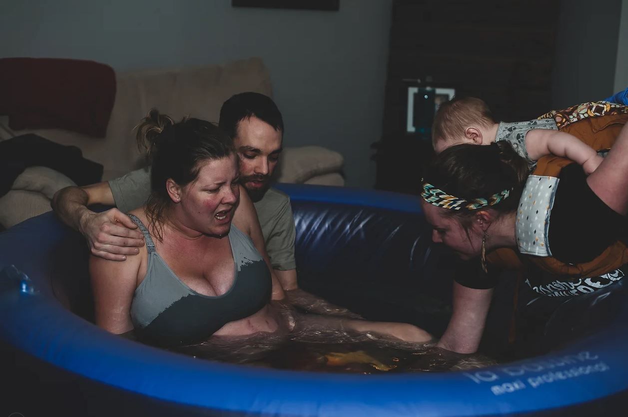 A powerful birthing scene with supporters gathered around a blue pool.