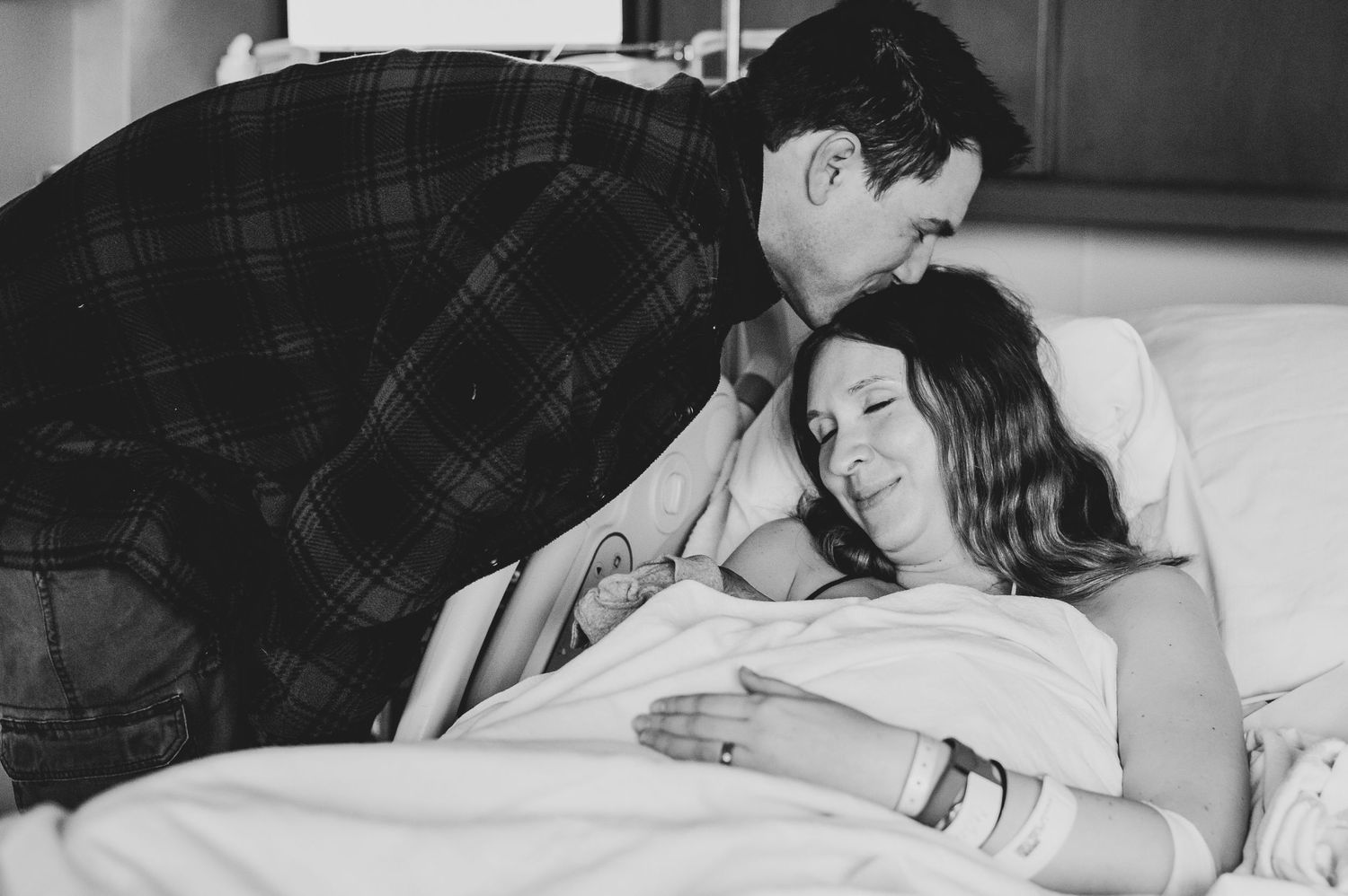 An intimate black and white photograph capturing a tender moment in the delivery room.