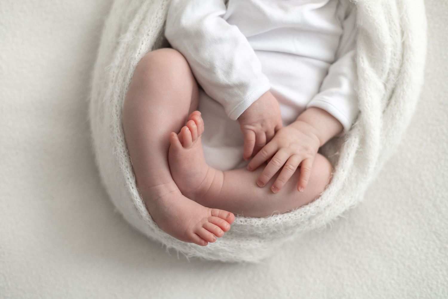 Close-up of a newborn baby's tiny feet and hands wrapped in a soft white blanket on a white background natural newborn photoshoot Nottingham