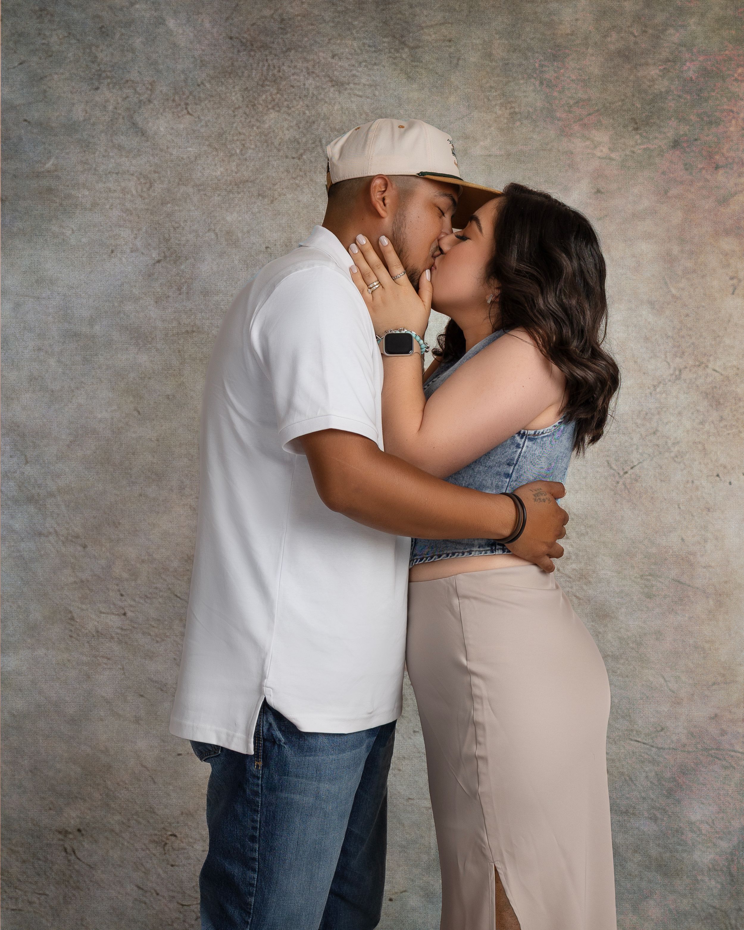 Couple sharing a romantic kiss during a professional studio portrait session with a neutral textured background.