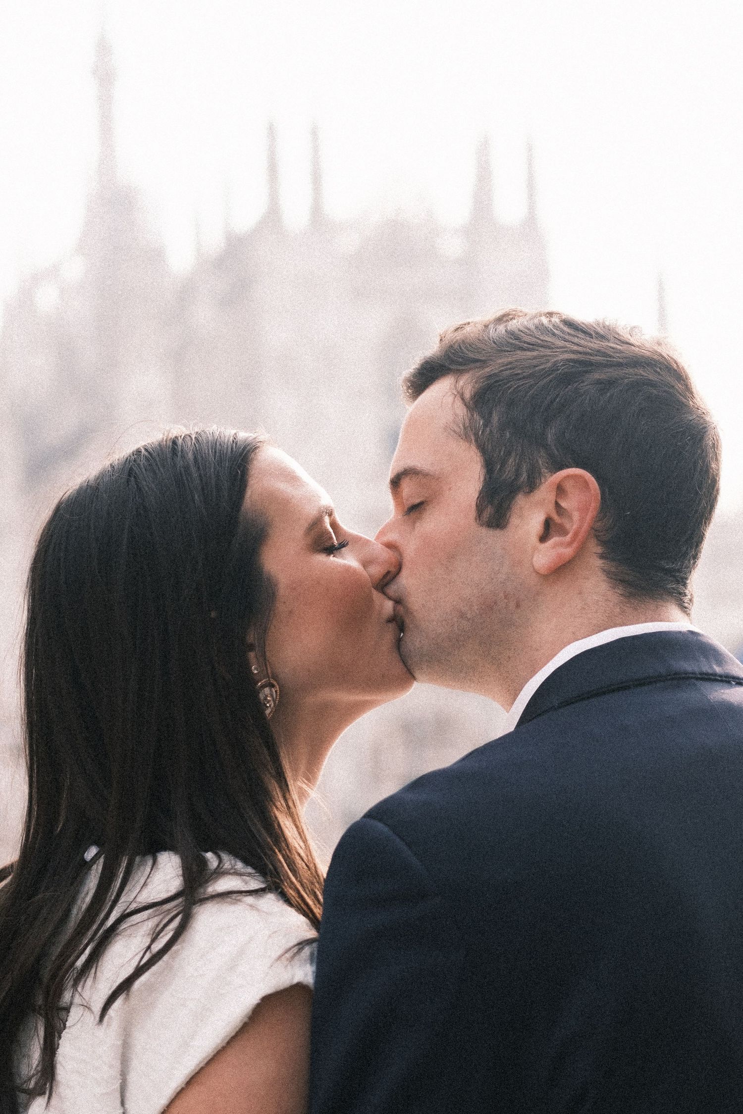 A couple shares a romantic kiss with the iconic Milan Cathedral in the soft-focus background.