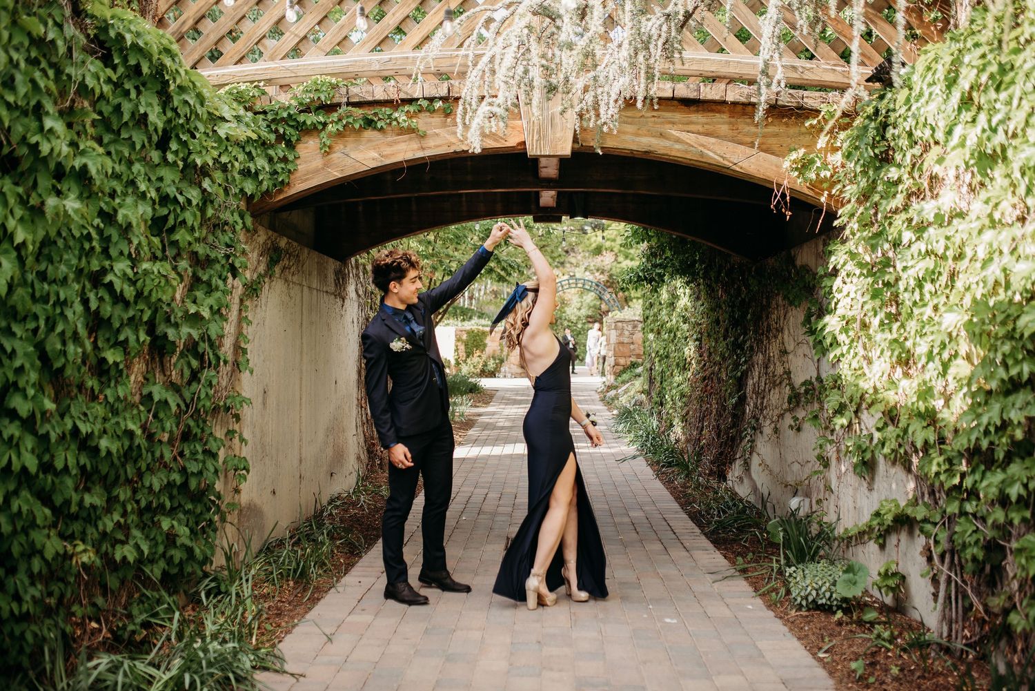 Couple in formal wear posing under an ivy-covered archway in an elegant garden setting.