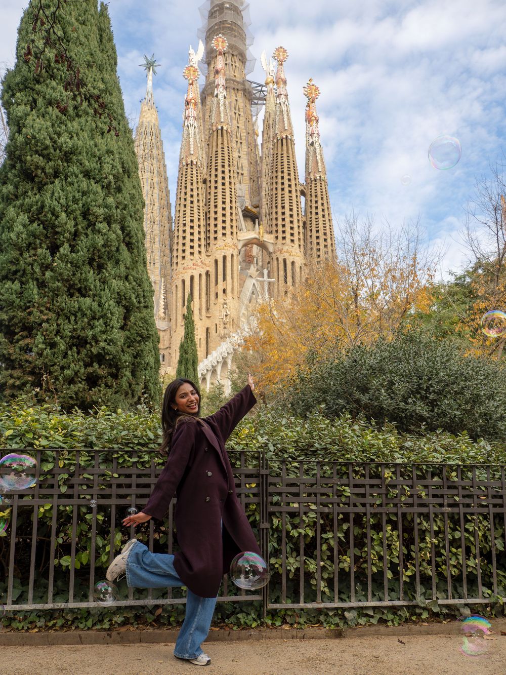 Tourist photo of a young girl at the Sagrada Familia in Barcelona with cypress trees in the foreground.