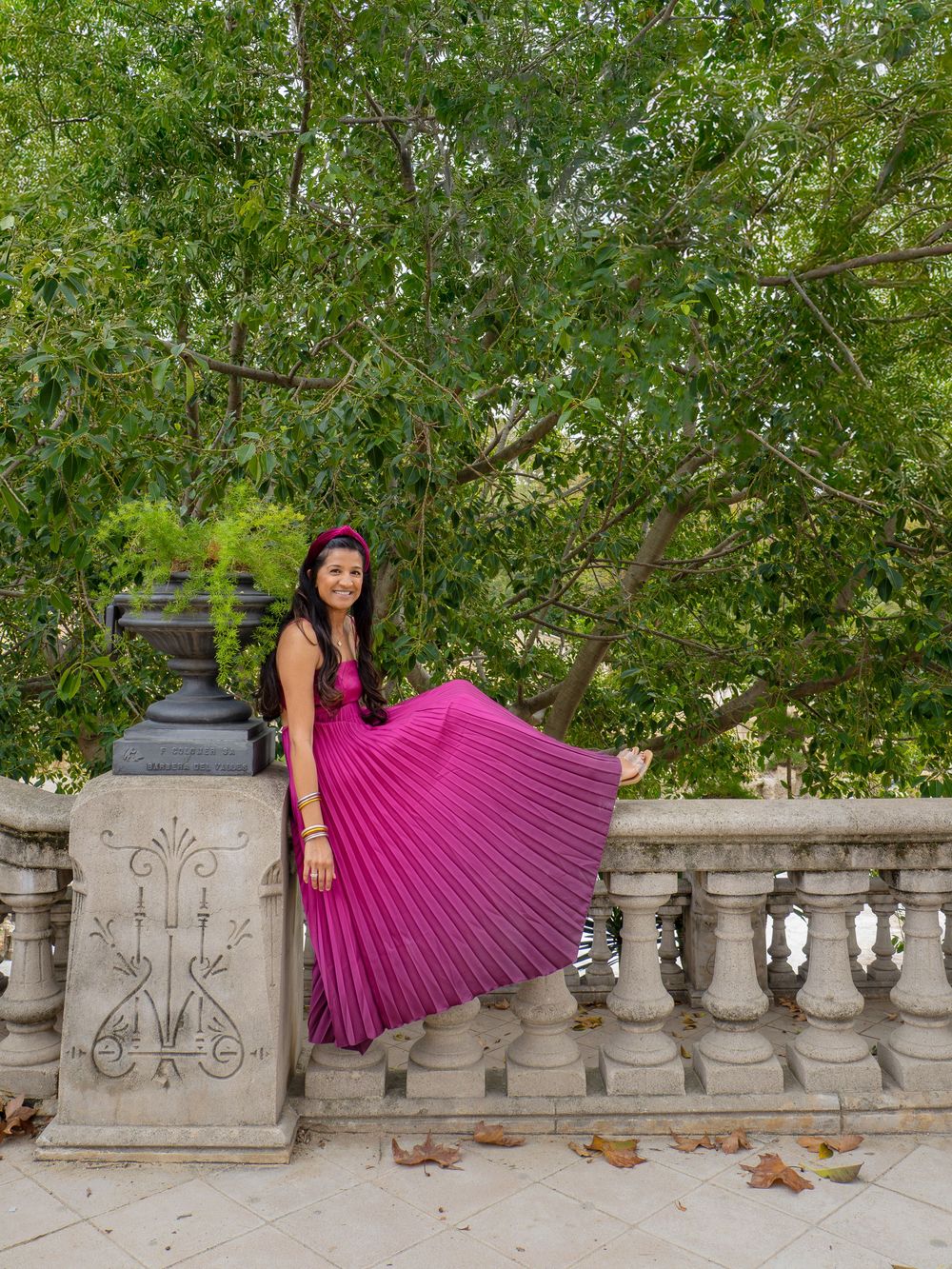 A woman wearing a flowing pink pleated skirt displayed against an ornate stone balustrade.