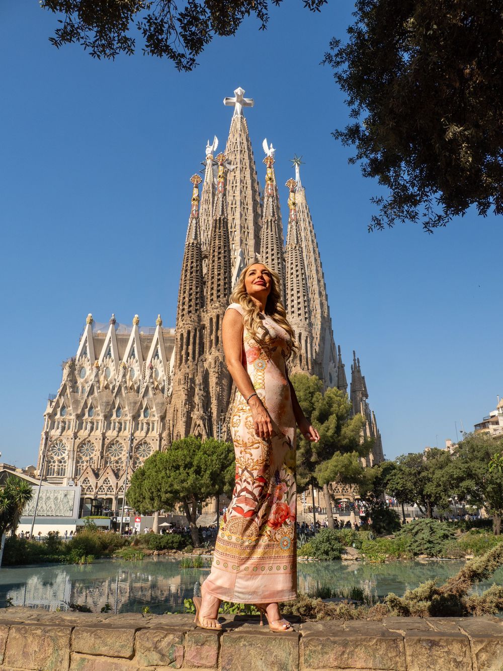 Woman in floral maxi dress posing in front of Sagrada Familia basilica in Barcelona on a sunny day.