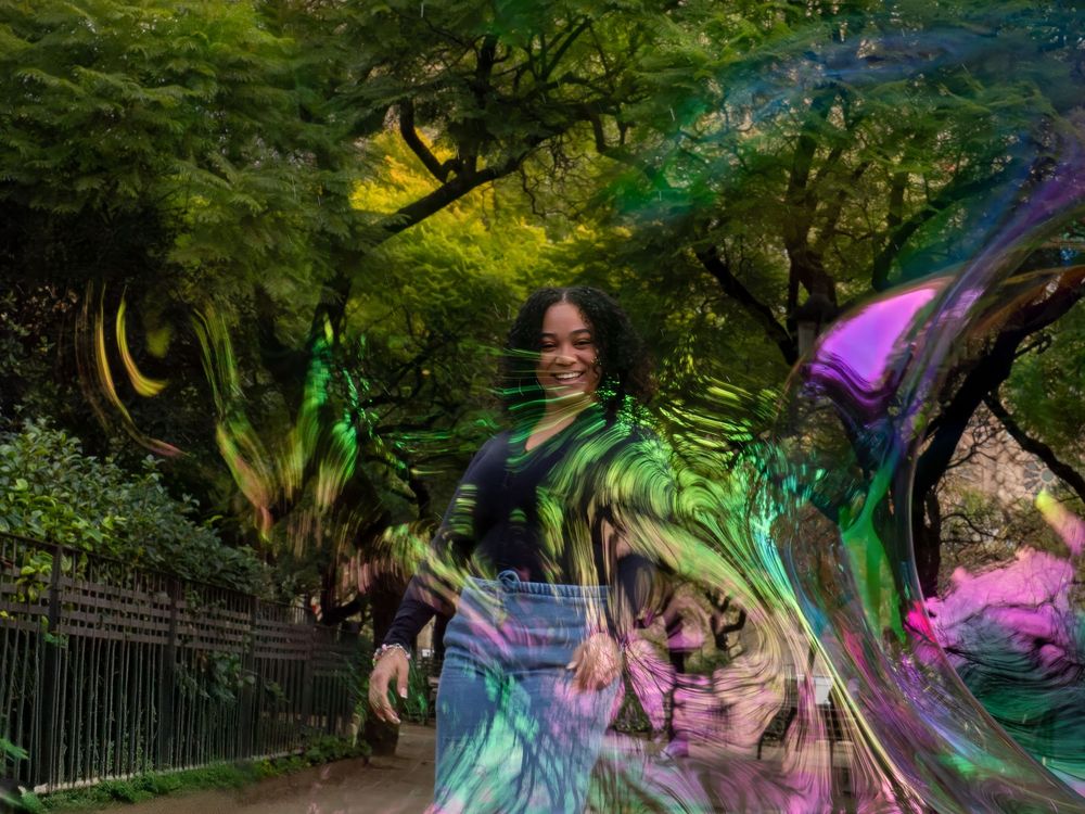 Artistic photo of a woman playing with soap bubbles in a garden setting.