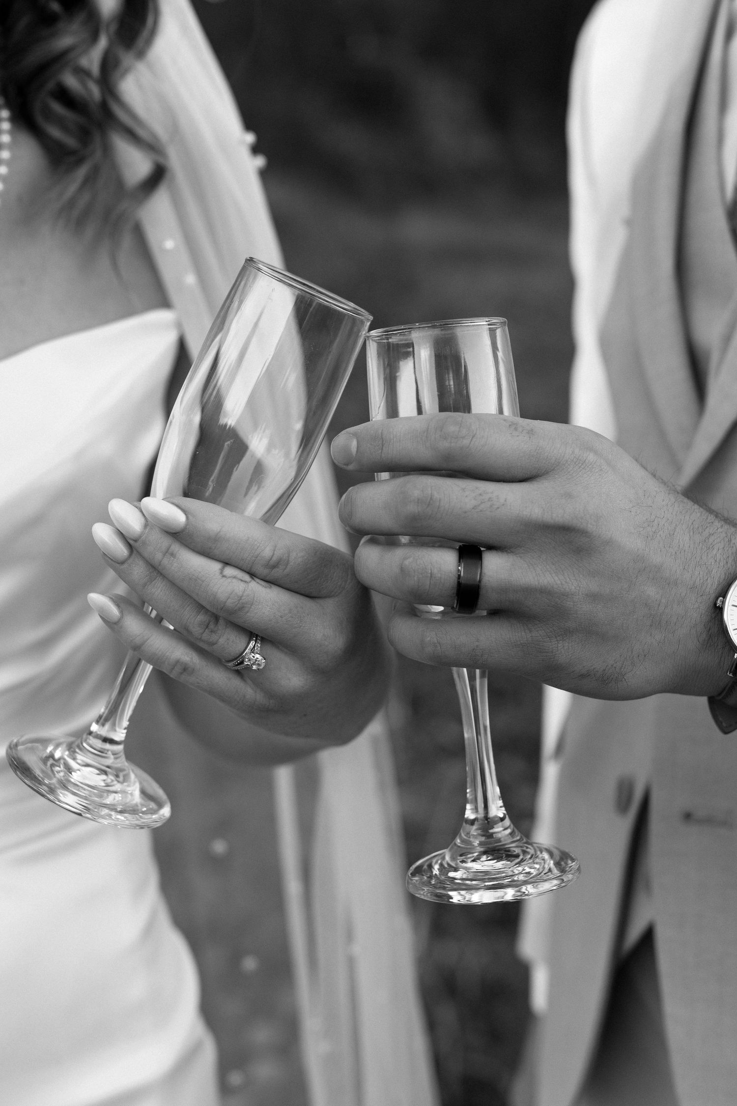 A black and white image showing hands holding champagne glasses, showing off wedding bands.
