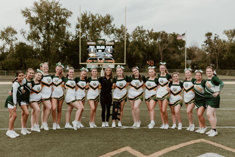 Cheerleading squad posing together on a football field in green and white uniforms.