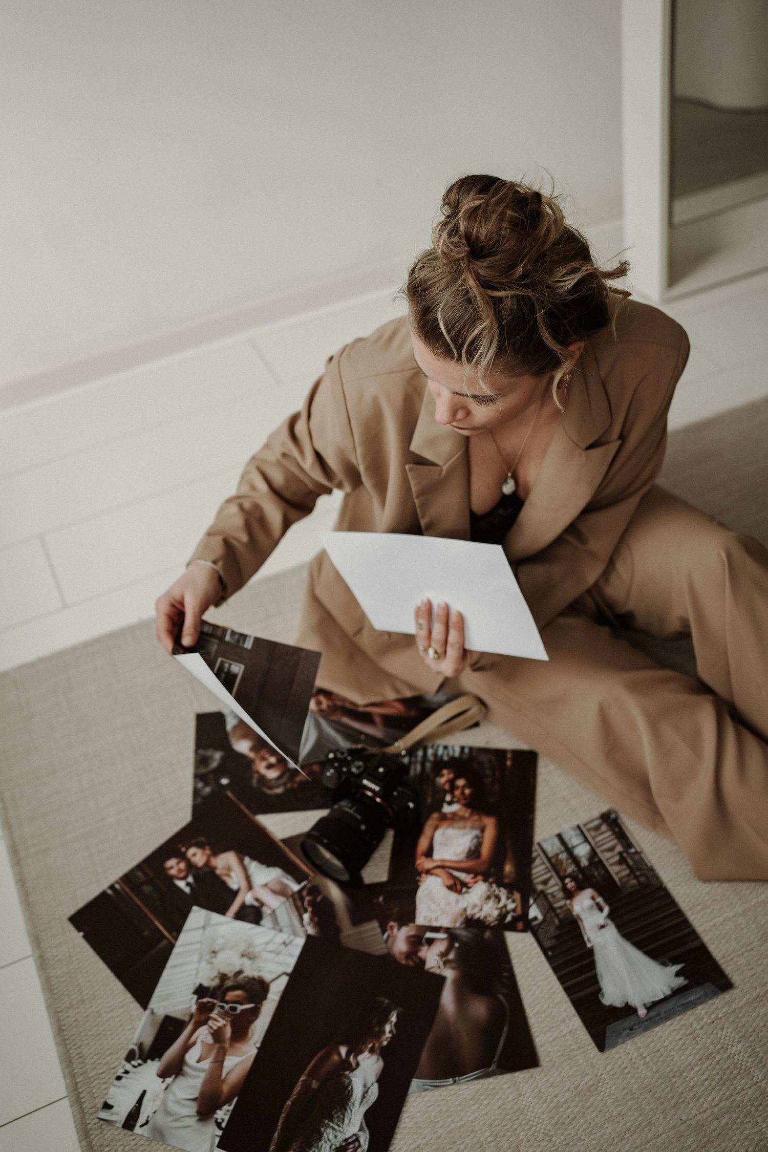 Someone in a tan coat sits on the floor looking through a collection of scattered wedding photographs.