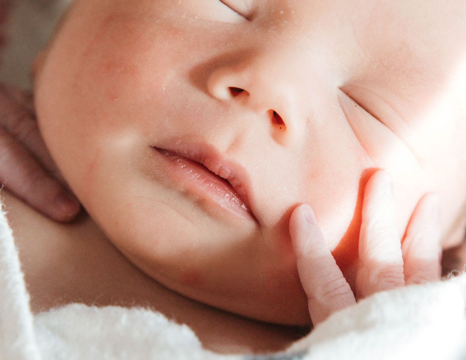 Close-up view of a sleeping baby's face with soft, rosy skin and peaceful expression.
