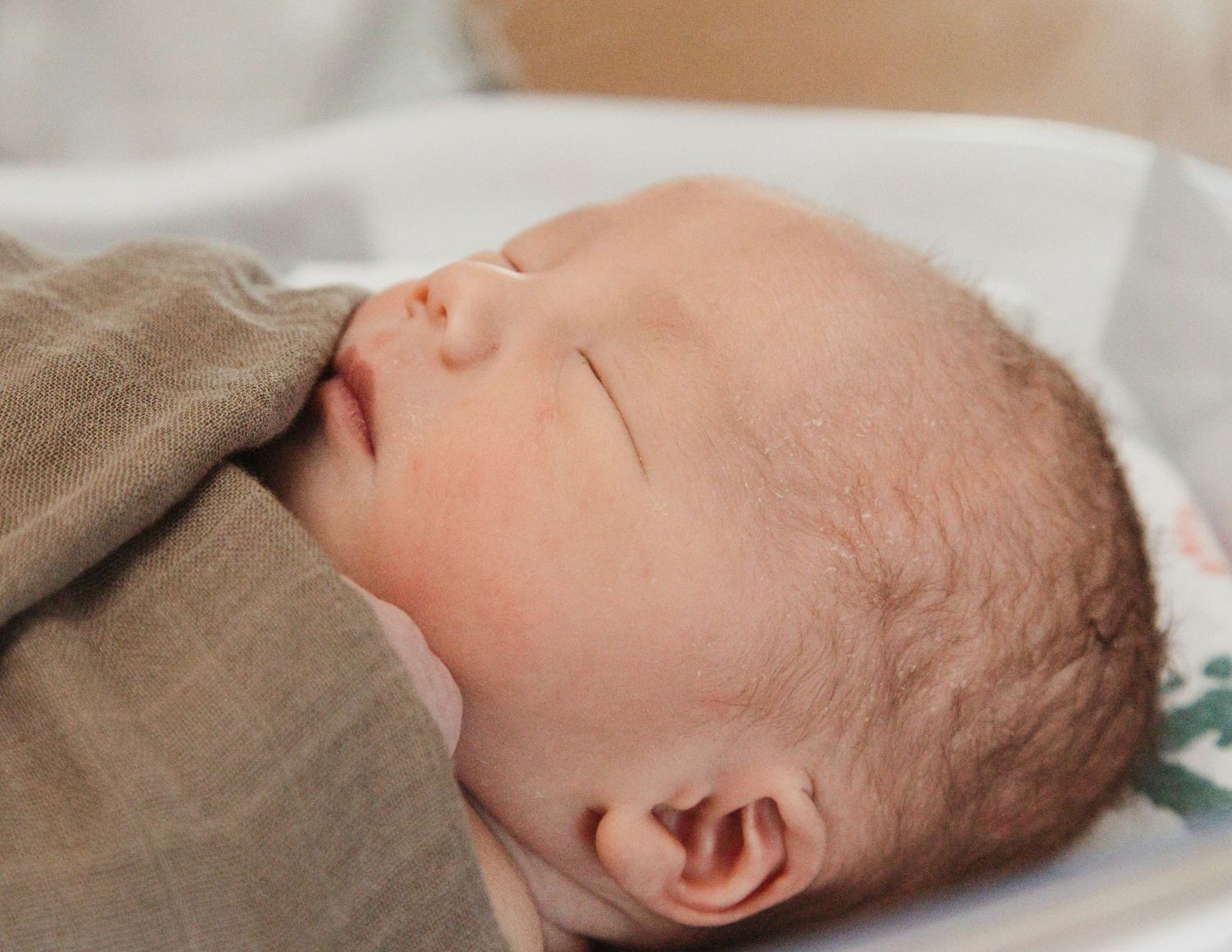 Close-up profile view of a sleeping infant swaddled in neutral-colored blankets.