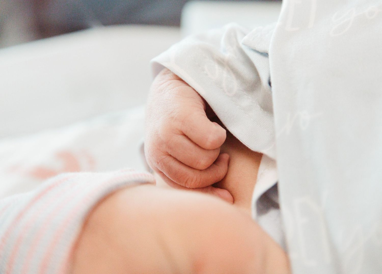 Small hand of a newborn baby grasping gently against white fabric background.