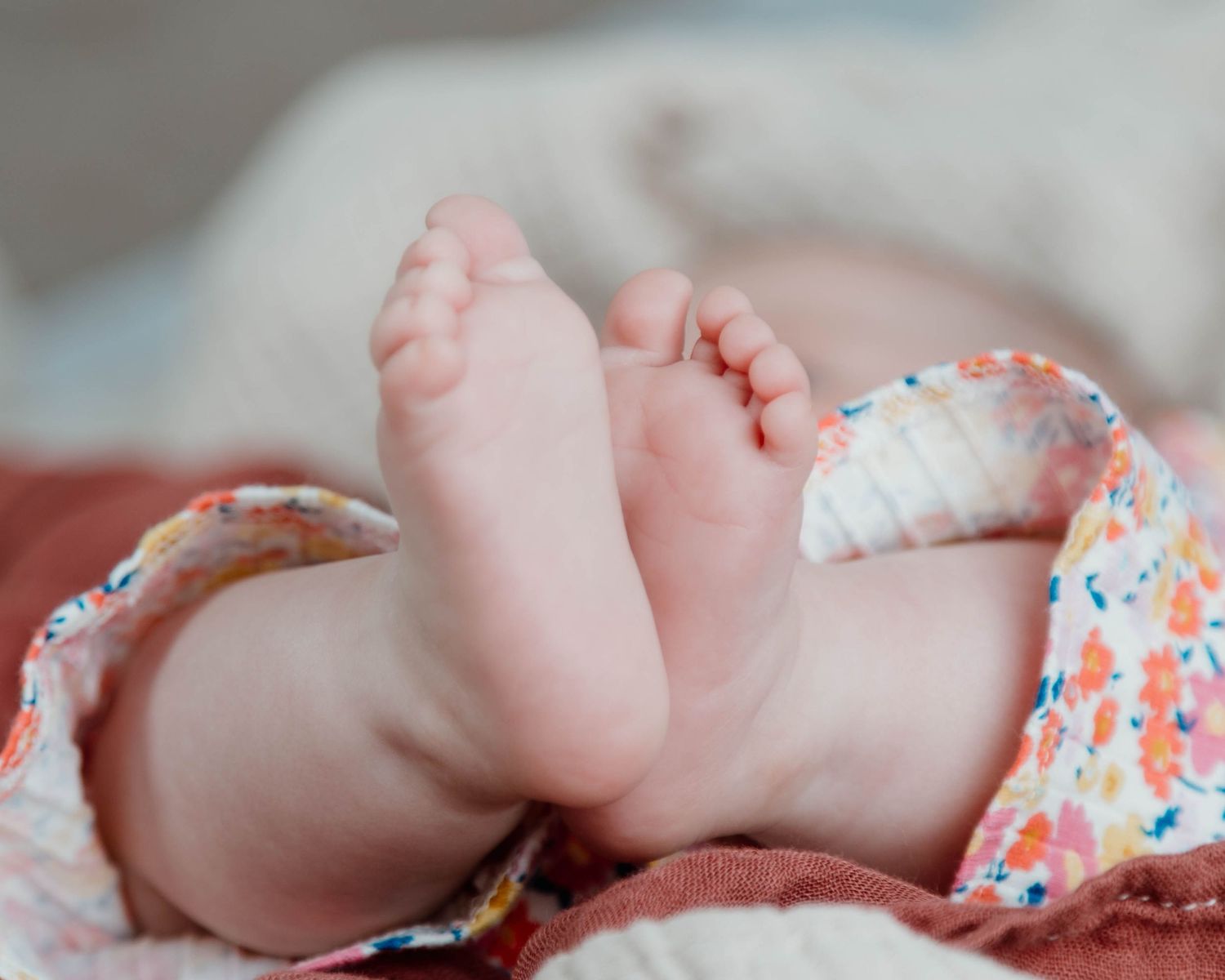 Close-up of tiny baby feet resting on a floral patterned blanket.
