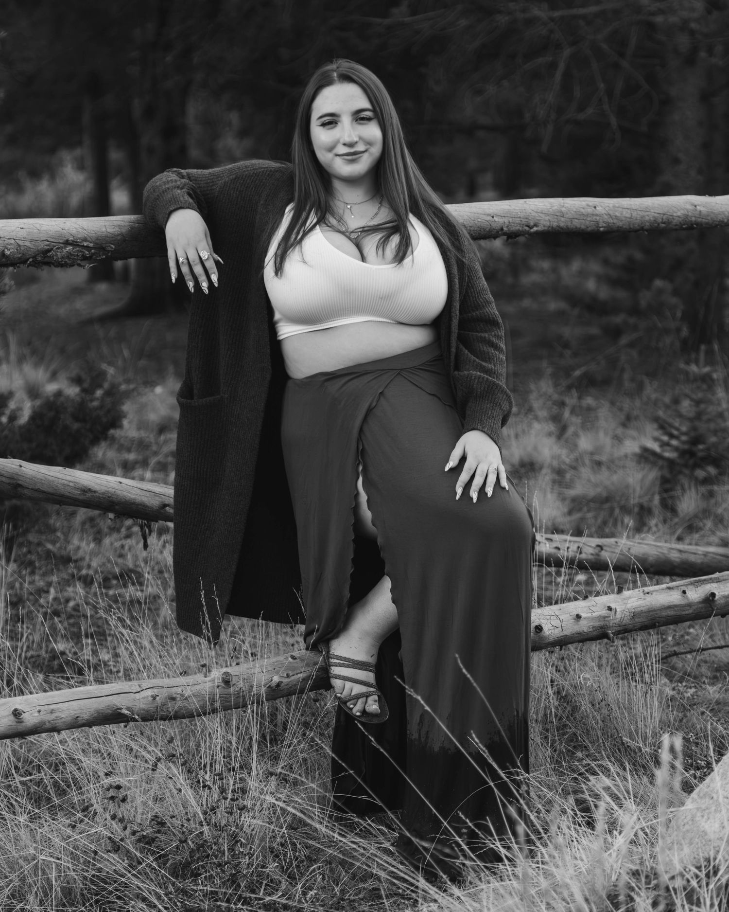 Black and white portrait of someone posing casually against a wooden fence wearing a crop top and long skirt.