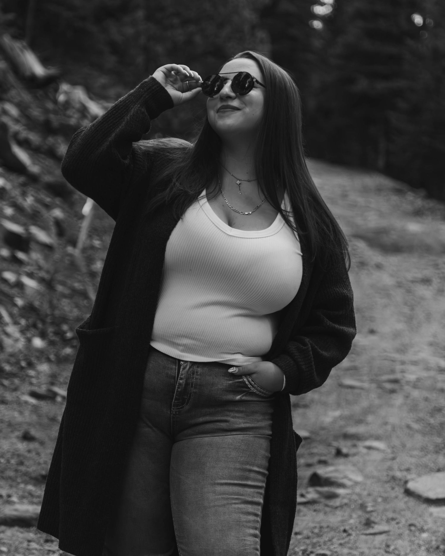 Black and white fashion portrait on forest trail featuring long cardigan and sunglasses.