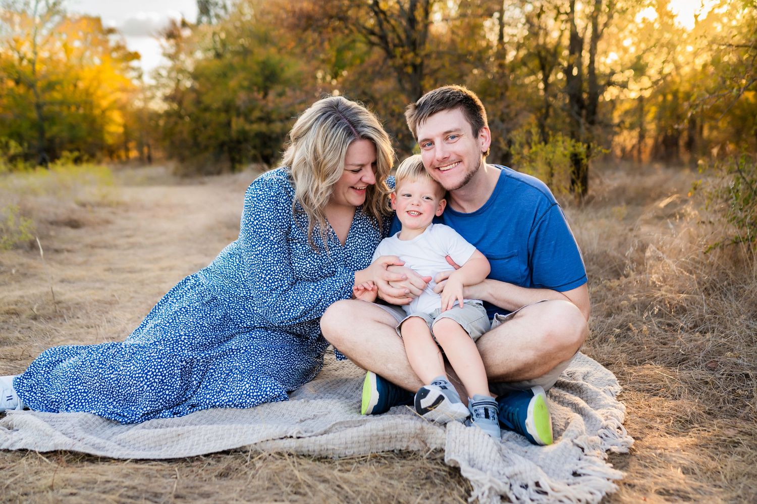 toddler son in fathers lap sitting on blanket getting tickled by mom during fall family photo session by mesquite tx family photographer
