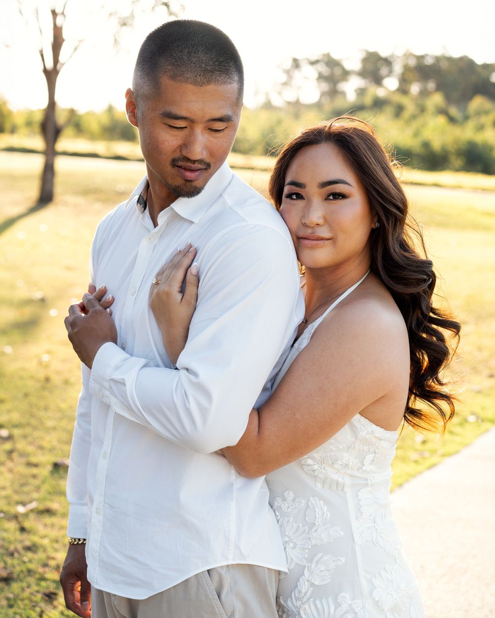 A romantic couple in white attire embraces during a sunset photoshoot.