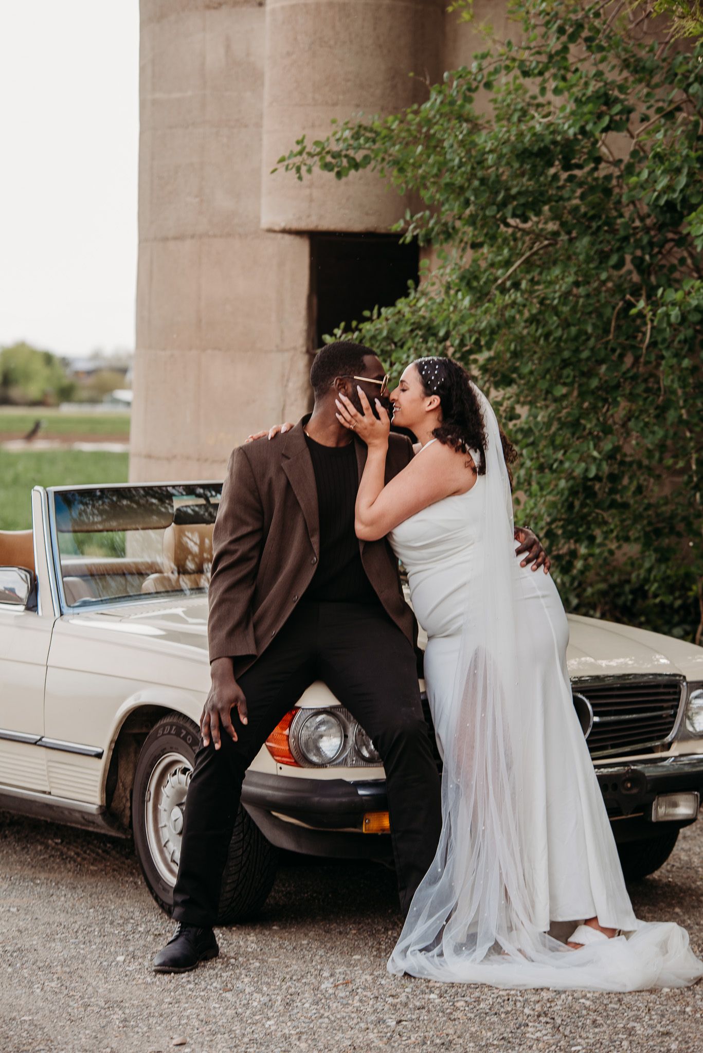 A romantic moment between newlyweds posed against a vintage car.