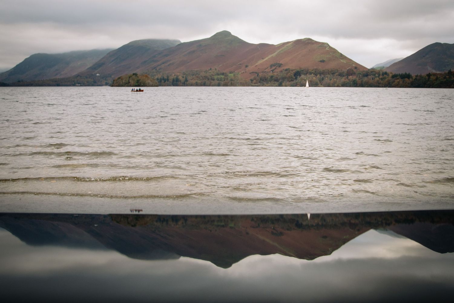 Mountains reflect perfectly in calm lake waters under an overcast sky.