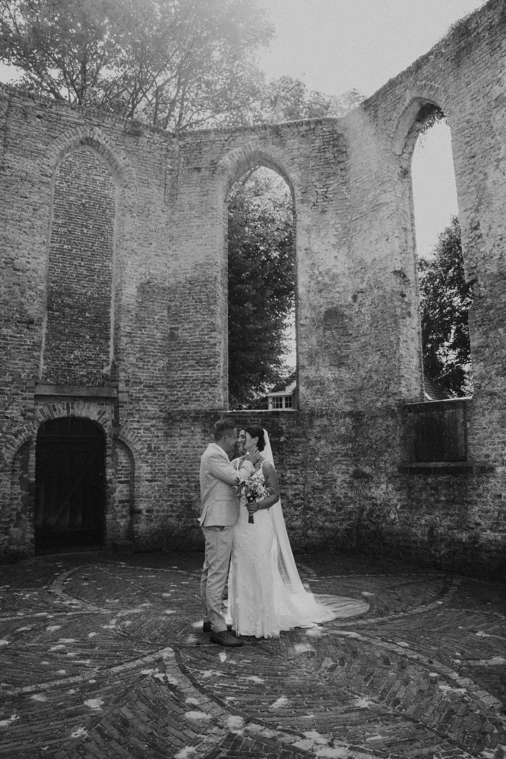 A couple shares an intimate moment in the stone ruins of an old church with gothic arched windows and weathered walls.