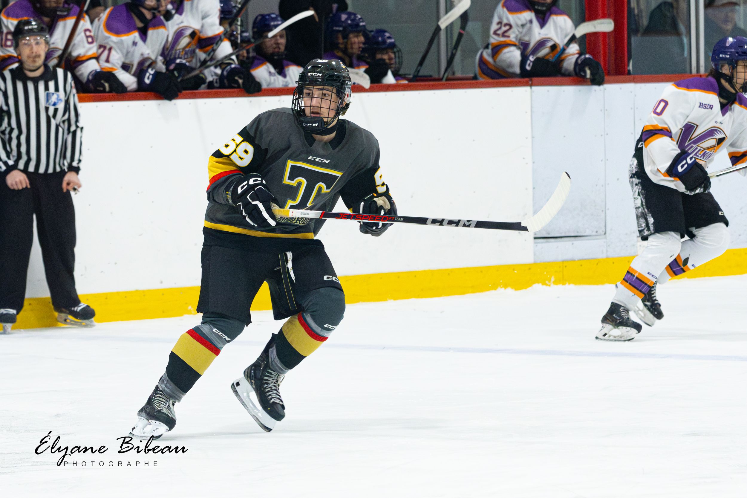Hockey player in dark uniform skates with puck during competitive match.