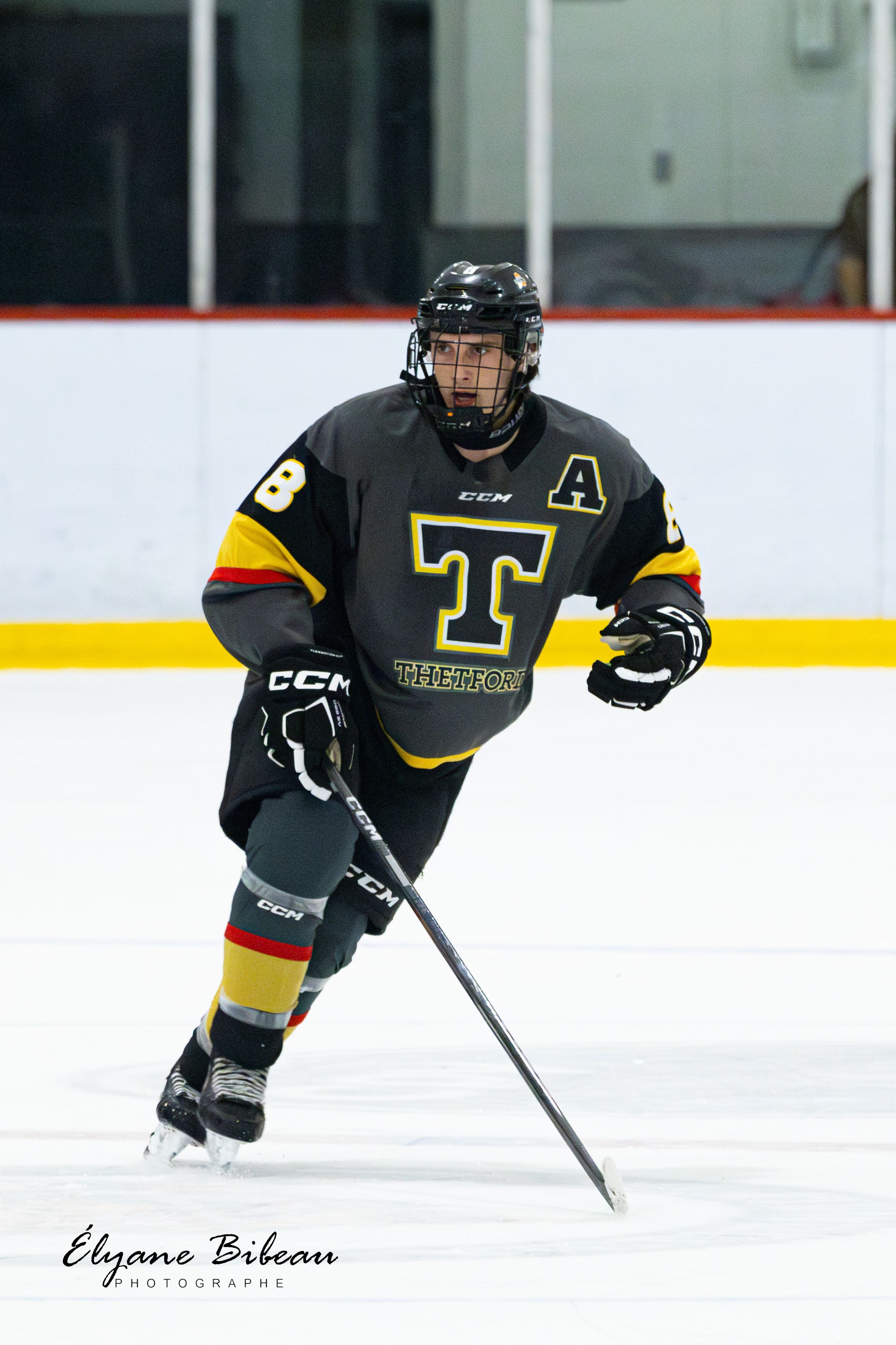 Hockey player in black and yellow uniform with number 98 and letter T skates on ice during game.