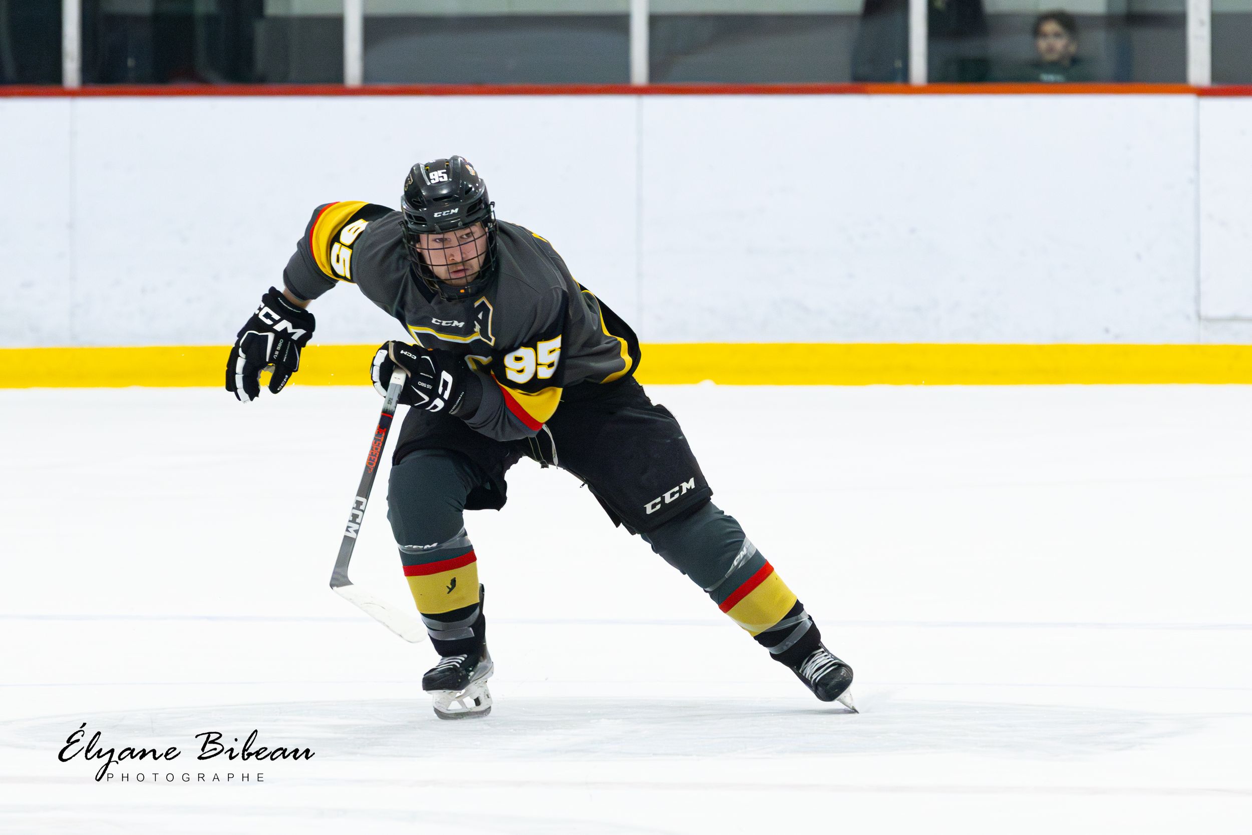 Hockey player in black uniform with yellow accents performs skating maneuver during game.