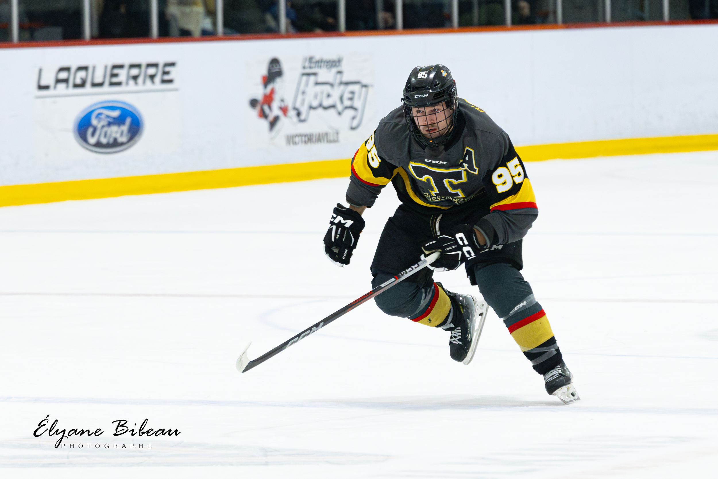 Hockey player wearing black and yellow uniform skates with stick during competitive match.