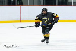 Ice hockey player in dark uniform with yellow stripes skates during competitive match.