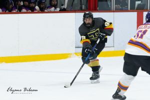 Hockey player in black uniform handles puck while opponent approaches during game.