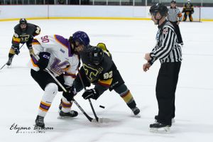 Hockey players face off at center ice with referee observing the play.