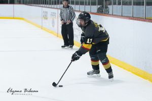Hockey player in dark uniform controls puck along the boards during game.