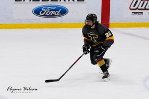 Hockey player in black and yellow uniform skates with puck on ice rink during game.