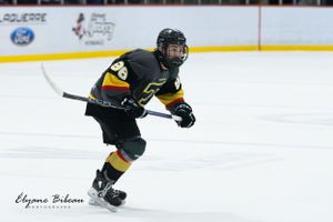 Hockey player in black and gold uniform controls puck while skating during match.