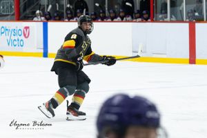 Hockey player in dark uniform skates with stick during ice hockey match.