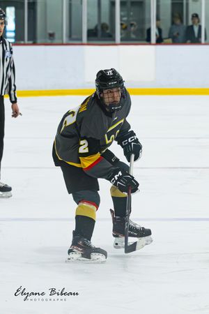 Hockey player in black and gold uniform positions for play near referee on ice.