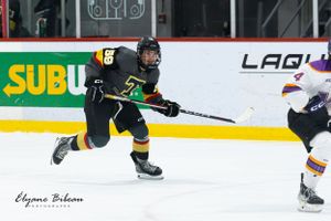 Hockey player in dark uniform races with puck during competitive game.