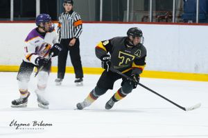 Hockey player in black jersey maneuvers past defender in white and blue uniform.