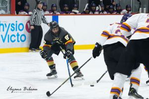 Hockey player in black and yellow jersey handles puck against defending opponents.