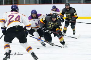 Hockey players in black and orange jerseys compete for the puck during an intense ice hockey match.