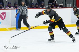 Ice hockey player in black and gold jersey skates with stick extended during game play.