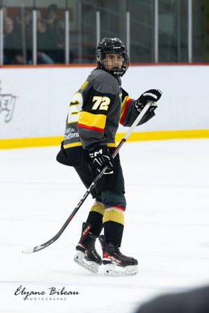 Hockey player in black and yellow uniform with number 72 stands ready on the ice.