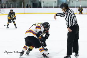 Ice hockey players battle for puck control during face-off as referee watches.