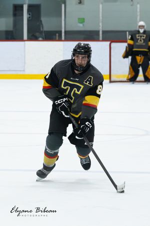 Hockey player in black jersey with letter A skates with puck on ice rink.