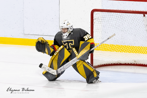 Goalie in black and gold uniform defends net during ice hockey game.